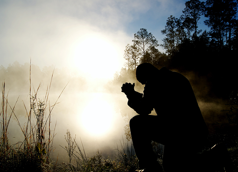 Man praying by a misty pond
